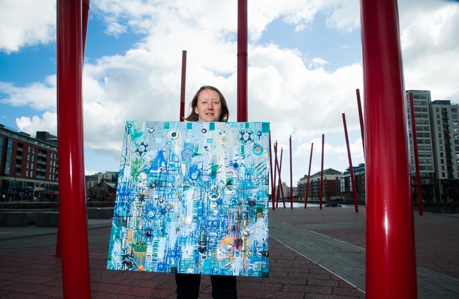 Catherine Ryan holding 'Blue City' painting at red poles, Grand Canal Dock. - Nua Collective - Artist