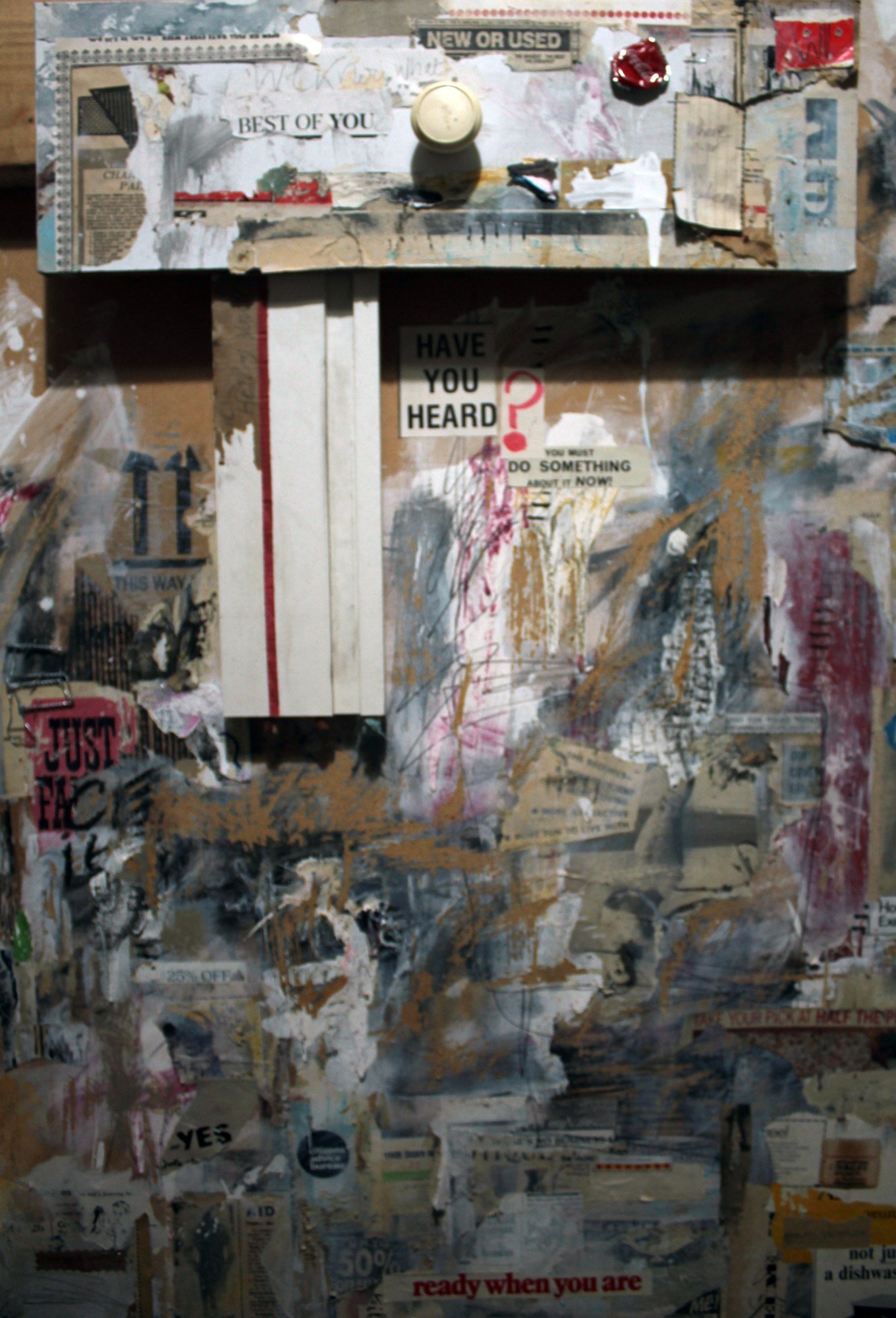 A sculptural collage built around a rectangular opening, with bottle caps and fragments of advertising above it.