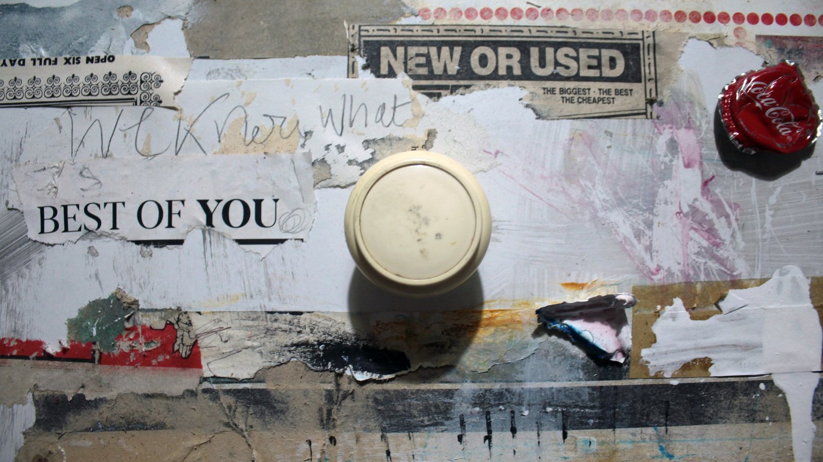 Detail of a collage with the phrases NEW OR USED and BEST OF YOU, a bottle cap and a projecting round object.