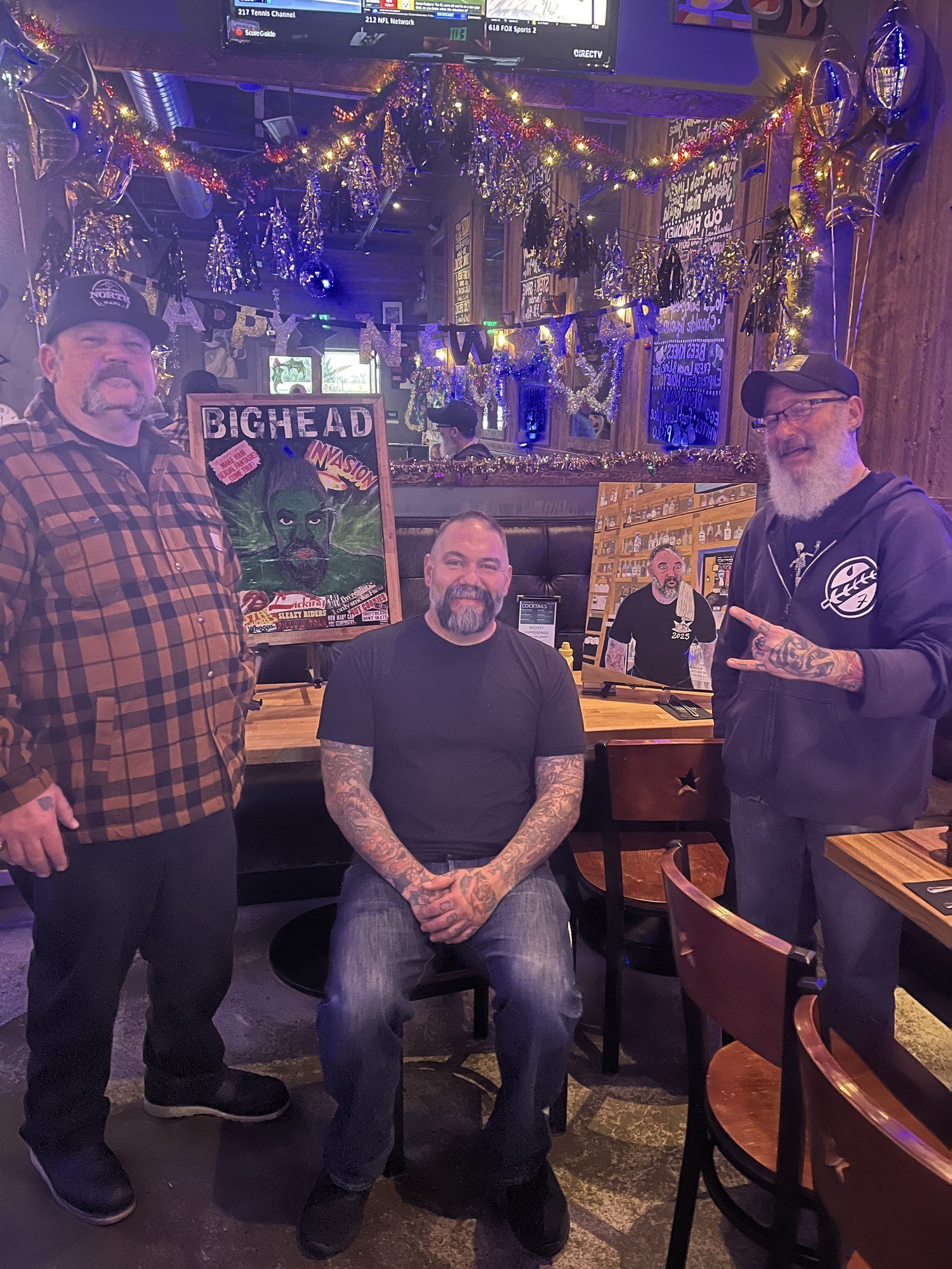 Two men pose beside the displayed portrait at the bar during the New Year’s Eve gathering.