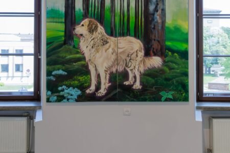 A painting of a pale dog in a green woodland displayed between gallery windows.